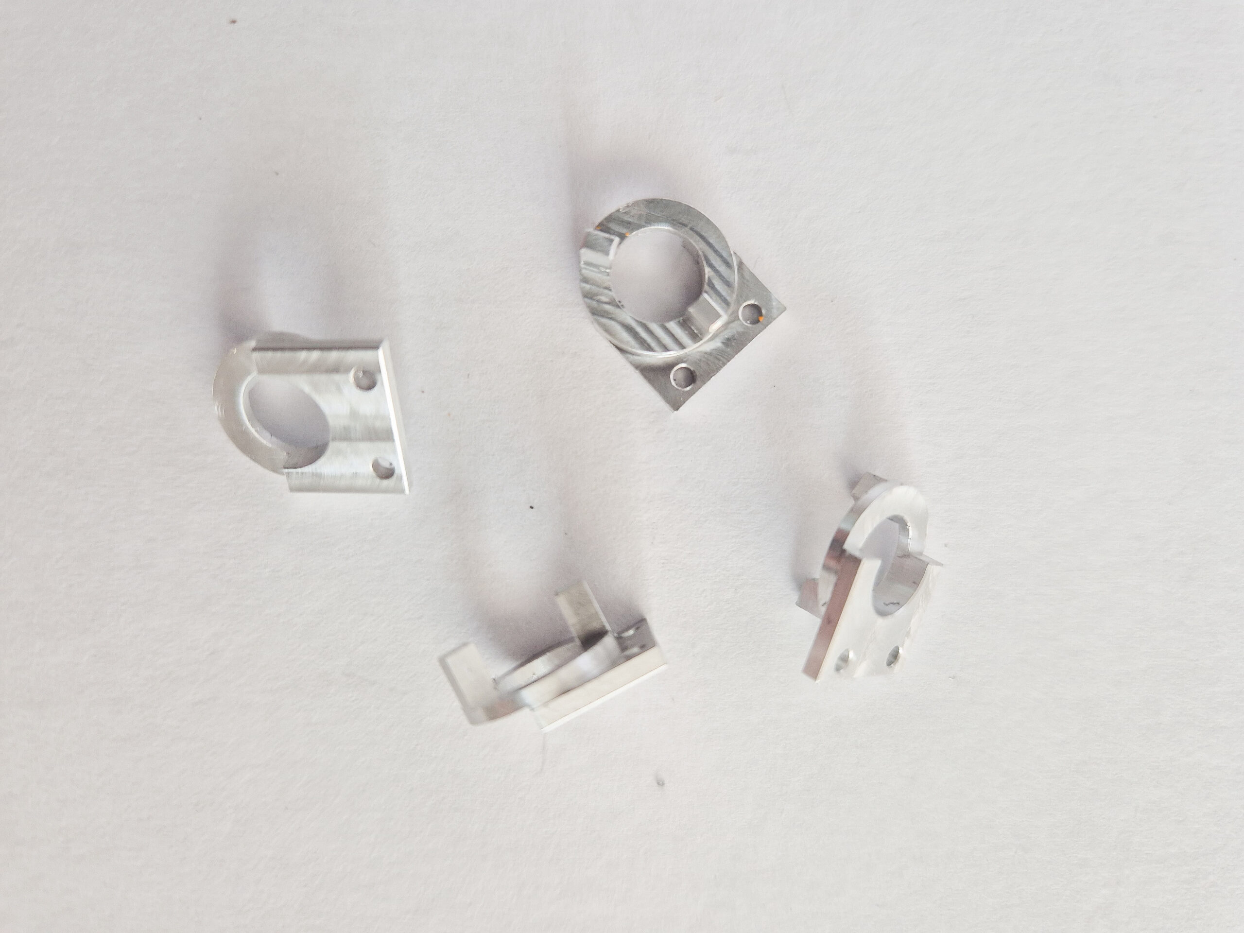 Quatre petites pièces métalliques usinées en aluminium, de forme semi-circulaire avec des trous de fixation